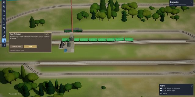 A long freight of green wagons on a line with a passing loop, a grey coal mine tower and the first-route guide on screen